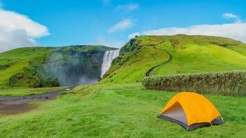 vue panoramique sur le camping avec tente orange et touristes devant la célèbre cascade de skogafoss, lors d'une randonnée en islande, été, vue panoramique.