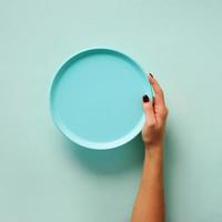 main féminine tenant une assiette bleue vide sur fond pastel