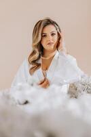 Matin de le la mariée avant le mariage. une magnifique Jeune femme avec une voile et une magnifique coiffure dans une blanc peignoir dans une pièce avec une magnifique intérieur. Naturel beauté et professionnel se maquiller. photo