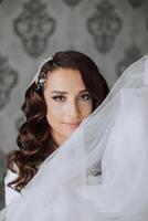 une magnifique brunette la mariée avec une tiare dans sa cheveux est avoir prêt pour le mariage dans une magnifique peignoir dans boudoir style. fermer mariage portrait, photo. photo