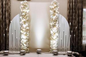 une magnifiquement décoré endroit pour le mariage la cérémonie de le la mariée et jeune marié dans une moderne style. mariage cambre fabriqué de blanc Frais fleurs. magnifique décoratif bougies. photo