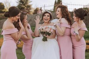 groupe portrait de le la mariée et demoiselles d'honneur. la mariée dans une mariage robe et demoiselles d'honneur dans rose ou poudre Robes et en portant élégant bouquets sur le mariage journée. photo