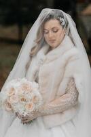 portrait de une magnifique la mariée avec une mariage bouquet de fleurs, attrayant femme dans une mariage robe avec une longue voile. content la mariée femme. la mariée avec mariage maquillage et coiffure. hiver mariage photo