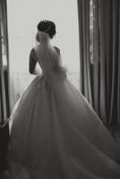 une luxueux la mariée avec une magnifique coiffure et une élégant robe, retour voir, est avoir prêt pour le mariage la cérémonie dans le Matin. Matin photo de le la mariée à Accueil ou dans une Hôtel chambre.