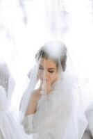 une magnifique brunette la mariée avec une tiare dans sa cheveux est avoir prêt pour le mariage dans une magnifique peignoir dans boudoir style. fermer mariage portrait, photo. photo