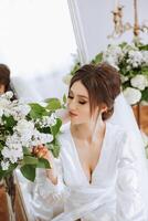 une magnifique brunette la mariée est avoir prêt pour le mariage dans une magnifique boudoir style tenue séance sur une chaise parmi Frais fleurs et élégant chandeliers. mariage portrait, photo. photo