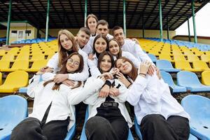 une groupe de beaucoup content adolescents habillé dans le même tenue ayant amusement et posant dans une stade près une collège. concept de amitié, des moments de Bonheur. école relation amicale photo