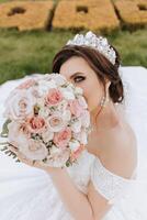 brunette la mariée dans hors de l'épaule dentelle blanc robe et tiare posant avec une bouquet de blanc et rose fleurs. magnifique cheveux et se maquiller. printemps mariage photo