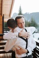 une père câlins le sien mature fils et aide lui préparer pour le mariage cérémonie. chaud et sincère rapports entre une père et un adulte fils. un émotif moment à une mariage photo