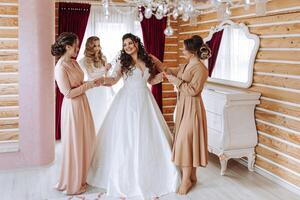 copains réjouir avec le la mariée dans le Matin. elles ou ils prendre des photos, sourire, Aidez-moi le la mariée boucler sa robe. photo