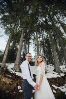 une Jeune couple, le la mariée et marié, en souriant spectacle de leur mariage anneaux contre le Contexte de grand des arbres. avoir une bien temps en riant. hiver mariage photo