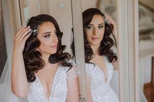 une magnifique magnifique portrait de une Jeune la mariée. magnifique la mariée avec mariage maquillage et bijoux couronne sur longue frisé cheveux. mariage photo modèle avec marron yeux dans une magnifique intérieur.