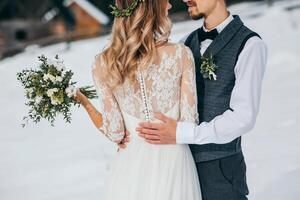 le jeune marié tendrement embrasse le sien magnifique la mariée. hiver mariage dans rustique style en plein air. tondu portrait, concentrer sur le de la mariée mariage robe. photo