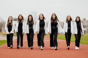 une groupe de beaucoup content adolescent les filles habillé dans le même tenue ayant amusement et posant dans une stade près une collège. concept de amitié, des moments de Bonheur. école relation amicale photo