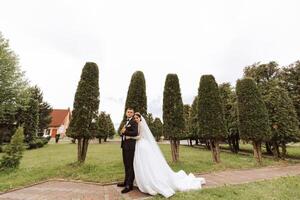 mariage. l'amour et couple dans jardin pour mariage. fête de la cérémonie et engagement. enregistrer le date. confiance. le la mariée et jeune marié embrasser. sourire et l'amour. le la mariée câlins le jeune marié par le épaules. photo