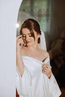 une magnifique brunette la mariée avec une tiare dans sa cheveux est avoir prêt pour le mariage dans une magnifique peignoir dans boudoir style. fermer mariage portrait, photo. photo