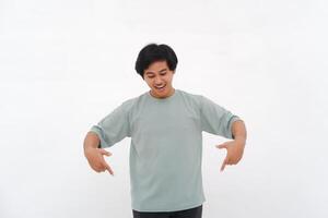 excité asiatique Masculin employé portant une T-shirt montrer du doigt à le copie espace au dessous de lui, isolé par une blanc Contexte photo