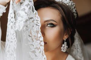 une magnifique brunette la mariée avec une tiare dans sa cheveux est avoir prêt pour le mariage dans une magnifique peignoir dans boudoir style. fermer mariage portrait, photo. photo