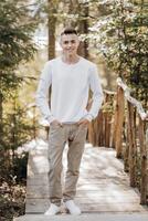 fermer verticale portrait de une adolescent dans une blanc chandail et marron pantalon. content souriant adolescent dans été parc dans lumière du soleil. une magnifique enfant est à la recherche à le caméra dans le clairière. photo