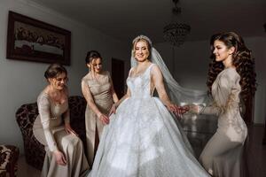 le la mariée dans une blanc robe, voile et copines dans crème Robes, posant dans magnifique éclairage. Matin de le la mariée photo