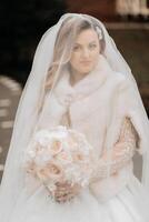 portrait de une magnifique la mariée avec une mariage bouquet de fleurs, attrayant femme dans une mariage robe avec une longue voile. content la mariée femme. la mariée avec mariage maquillage et coiffure. hiver mariage photo