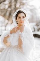 portrait de une magnifique la mariée avec une mariage bouquet de fleurs, attrayant femme dans une mariage robe avec une longue voile. content la mariée femme. la mariée avec mariage maquillage et coiffure. hiver mariage photo