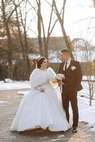 hiver mariage. content couple en marchant dans mariage vêtements étreindre et souriant dans une hiver parc couvert avec neige sur leur mariage journée. hiver l'amour récit de une magnifique couple dans neigeux hiver temps photo