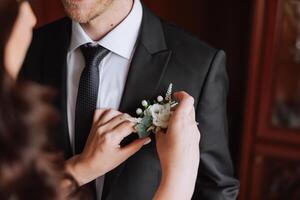 le la mariée s'accroche une boutonnière de des roses à le du marié veste photo