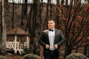 portrait de une Beau et viril jeune marié dans une noir costume avec une cravate. jeune marié dans la nature dans le hiver saison. photo
