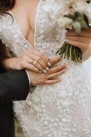 fermer de le du marié main embrassement le la mariée. le la mariée détient le du marié main. ouvert buste sur le de la mariée robe. photo