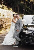 jeunes mariés près le noir mariage voiture supporter sur le route dans le été forêt. photo