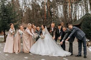 la mariée et jeune marié étreindre, posant avec amis. copains sont ayant amusement. content des moments. mariage portrait dans nature, mariage photo dans lumière couleurs.