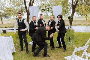 joyeux, jeune, énergique les témoins de le jeune marié suivant à le jeune marié. copains féliciter le jeune marié. jeune marié et le sien marrant copains ayant amusement sur le mariage journée de le jeunes mariés. photo