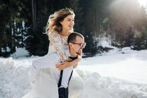 le la mariée et jeune marié sont fonctionnement le long de une neigeux route contre le Contexte de une pin forêt et magnifique contraste lumière du soleil. côté voir. hiver mariage. endroit pour logo. photo