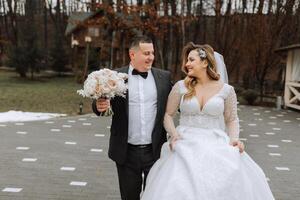 le la mariée et jeune marié sont en marchant près le Hôtel et poser, content et profiter le jour, en portant mains. une longue train sur le robe. hiver mariage photo