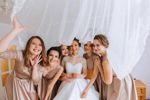 le la mariée dans une blanc élégant robe pose avec sa copines, couvrant se avec une voile photo