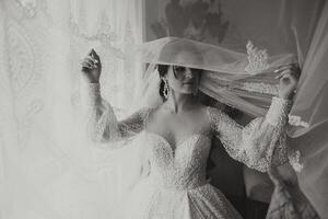 une luxueux la mariée avec une magnifique coiffure et une magnifique robe est avoir prêt pour le mariage la cérémonie dans le Matin. Matin photo de le la mariée à Accueil ou dans une Hôtel chambre. professionnel se maquiller.