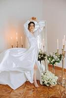 une magnifique brunette la mariée est en train de préparer pour le mariage dans une magnifique boudoir style robe parmi Frais fleurs et élégant chandeliers contre une miroir Contexte. mariage portrait, photo. photo