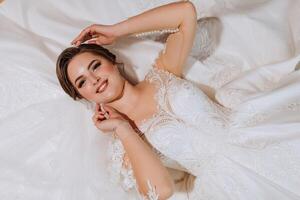 magnifique mariée, attrayant femme dans mariage robe, mensonge sur lit. à la mode coiffure et se maquiller. content la mariée femme. souriant la mariée. mariage journée. une magnifique la mariée. mariage. photo