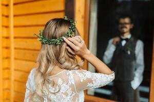 le premier réunion de le la mariée et jeune marié. il regards à son. de la mariée coiffure, retour voir, couronne de verdure sur le de la mariée tête photo