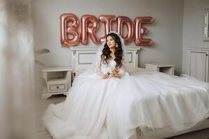 une magnifique magnifique portrait de une Jeune la mariée. magnifique la mariée avec mariage maquillage et bijoux couronne sur longue frisé cheveux. mariage photo modèle avec marron yeux dans une magnifique intérieur.