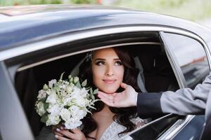 une magnifique mariée, séance dans une voiture, regards en dehors de le ouvert fenêtre de le auto. une magnifique la mariée avec une bouquet de fleurs dans sa mains est séance dans une élégant coûteux auto. photo