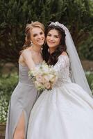 groupe portrait de le la mariée et demoiselles d'honneur. une la mariée dans une mariage robe et une demoiselle d'honneur dans une argent robe tenir une élégant bouquet sur leur mariage journée. photo