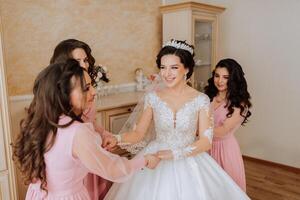 une ami aide le la mariée boucler sa robe. une femme aide sa ami boucler le boutons sur le retour de sa mariage robe. le Matin de le mariée, le création de une famille, un important événement. photo