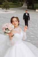 magnifique Jeune la mariée dans été parc permanent dans de face de sa marié, photo avec sélectif se concentrer. magnifique mariage blanc robe. des promenades dans le parc. une content et aimant couple.