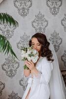 une magnifique brunette la mariée avec une tiare dans sa cheveux est avoir prêt pour le mariage dans une magnifique peignoir dans boudoir style. fermer mariage portrait, photo. photo