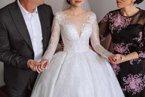 content Parents tenir le mains de le la mariée qui est avoir marié et soutien son, portant une mariage robe et une longue voile. photo