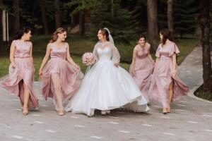 groupe portrait de le la mariée et demoiselles d'honneur. la mariée dans une mariage robe et demoiselles d'honneur dans rose ou poudre Robes et en portant élégant bouquets sur le mariage journée. photo