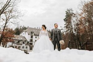 portrait. le la mariée et jeune marié marcher et pose tandis que en portant mains. une longue train sur le robe. hiver mariage photo