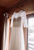 une parfait mariage robe avec dentelle manches sur une cintre dans le de la mariée chambre. préparation de le la mariée pour le mariage photo